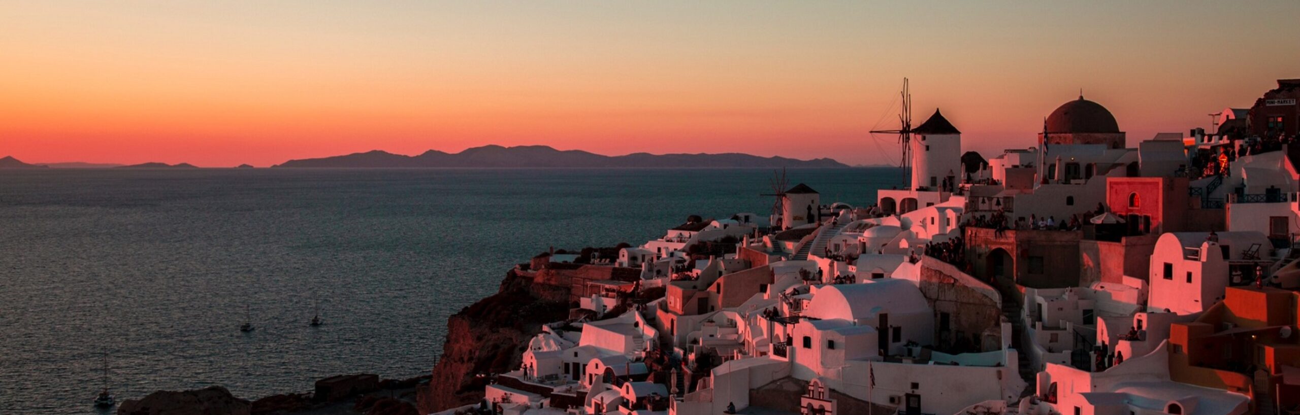 Sunset in Santorini: white buildings on the right bask in beautiful evening light, looking over the sea with land beyond